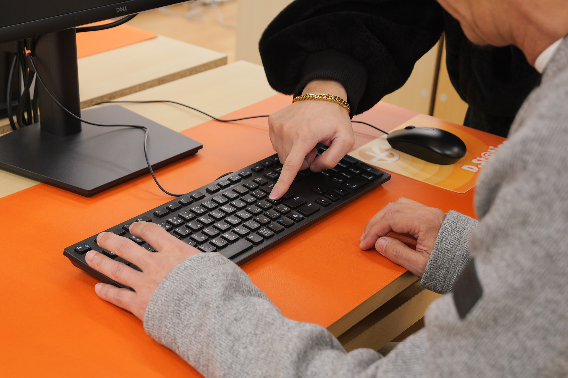 講師が生徒のキーボードを指差し、どのキーを打ち込むかを教えている様子