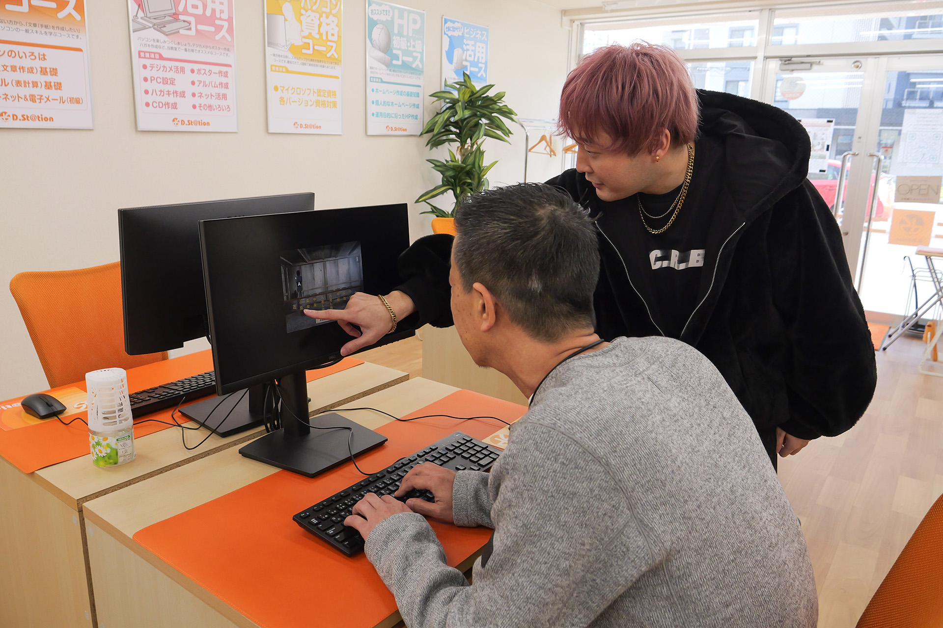 講師が生徒のパソコンのディスプレイを指差し、画面の説明をしている様子